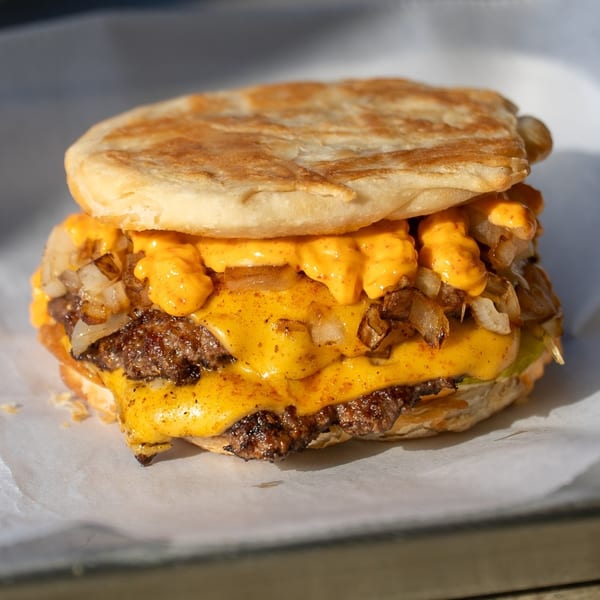 Close-up of a Sumah Hot Chicken burger with melted cheese, grilled onions, and special sauce.