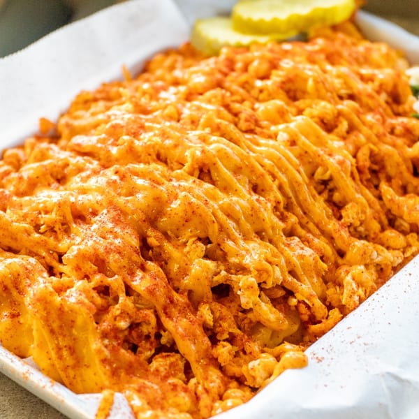 Sumah Hot Chicken's golden-brown waffle fries, generously topped with melted cheese sauce and sprinkled with seasoning.
